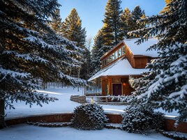 Una cabaña de madera con un frente de vidrio, rodeada de árboles cubiertos de nieve.