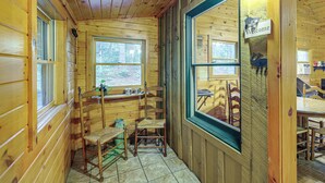 A wooden cabin interior with a dining area, a window with a 'Welcome' sign, and a view of the forest outside. - Rustic Cabin w/ Phoenix Mtn Views & Trail Access! (Lansing)