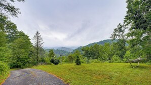 A rural road curving through a grassy landscape with trees and a hammock on the right. - Rustic Cabin w/ Phoenix Mtn Views & Trail Access! (Lansing)