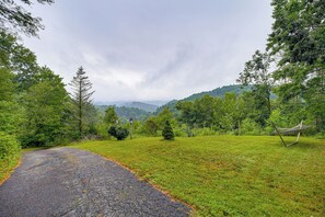 A rural road curving through a grassy landscape with trees and a hammock on the right. - Rustic Cabin w/ Phoenix Mtn Views & Trail Access! (Lansing)