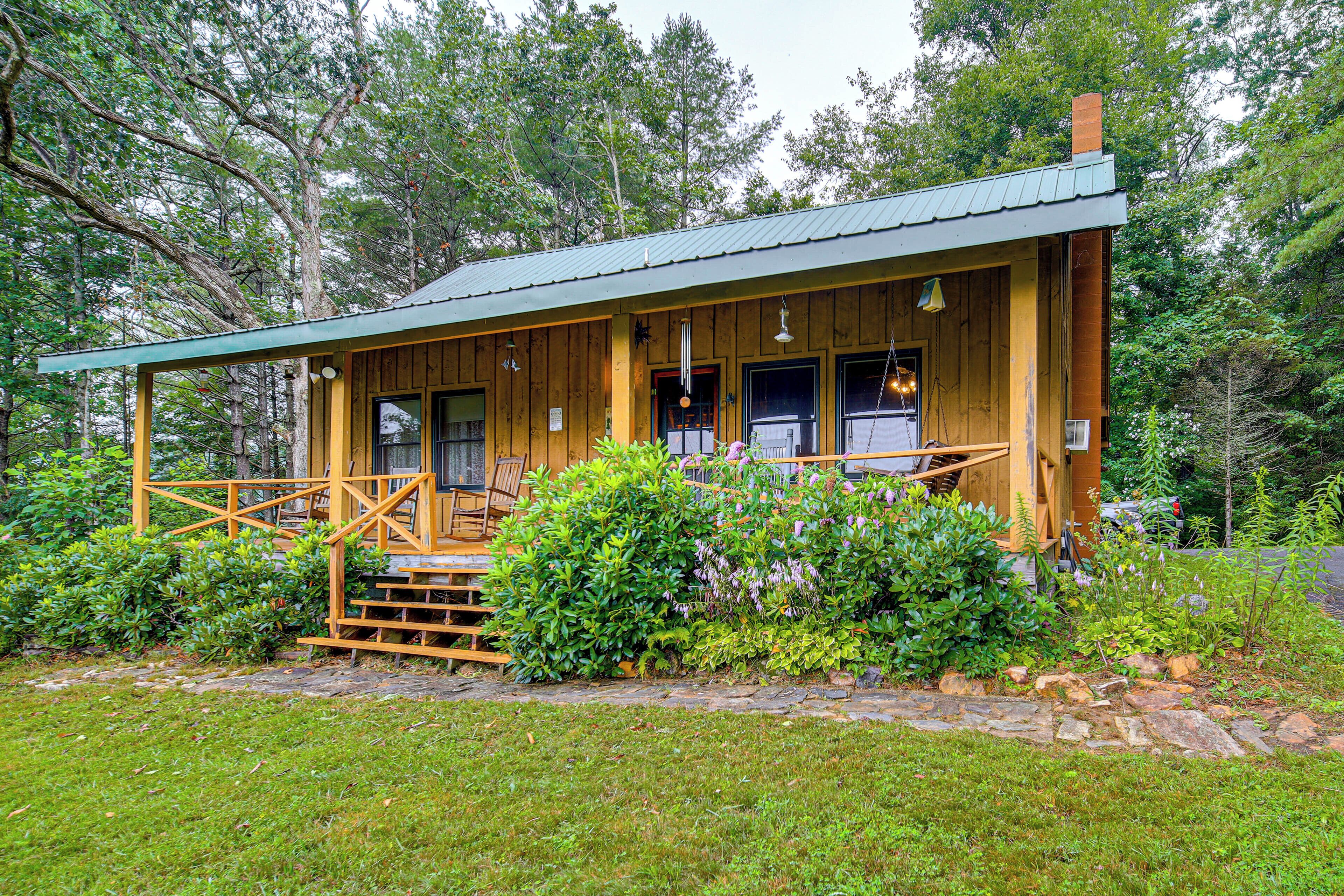 A wooden cabin with a porch, surrounded by lush greenery.