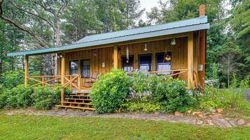 A wooden cabin with a porch, surrounded by lush greenery.