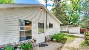 A single-story house with a front door, two windows, a stone foundation, and a small porch area. - Waterfront Escape on Bass Lake: Paddle, Fish, Swim (Irons)