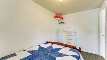 A bedroom with a bed, a white dresser, a wall-mounted clothes rack, and a door.
