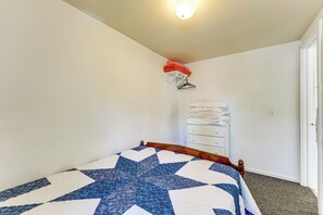 A bedroom with a bed, a white dresser, a wall-mounted clothes rack, and a door. - Waterfront Escape on Bass Lake: Paddle, Fish, Swim (Irons)