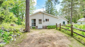 A single-story building with a dirt driveway, surrounded by trees and a wooden fence.