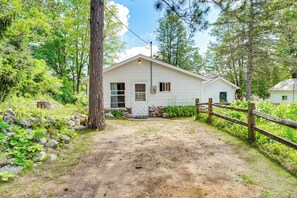 A single-story building with a dirt driveway, surrounded by trees and a wooden fence. - Waterfront Escape on Bass Lake: Paddle, Fish, Swim (Irons)