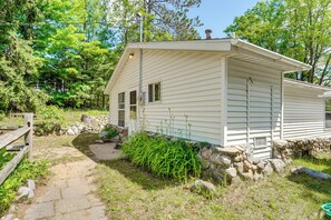 A single-story house with a stone foundation, a wooden deck, and a stone wall. - Waterfront Escape on Bass Lake: Paddle, Fish, Swim (Irons)
