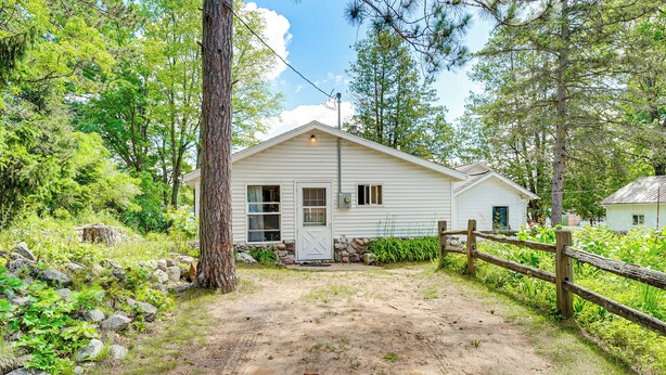 A single-story building with a dirt driveway, surrounded by trees and a wooden fence. - Waterfront Escape on Bass Lake: Paddle, Fish, Swim (Irons)