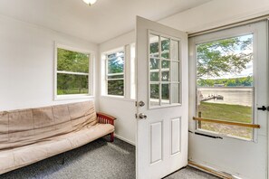 A room with a beige sofa, a white door with a view of a lake, and a small wooden stool. - Waterfront Escape on Bass Lake: Paddle, Fish, Swim (Irons)