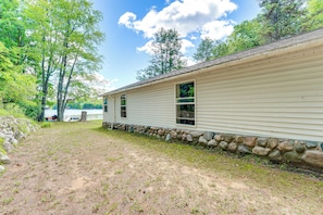 A single-story house with a stone foundation, a dirt yard, and a view of a lake.
