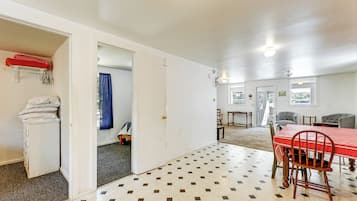 A room with a dining table, chairs, a white wardrobe, and a red tablecloth.