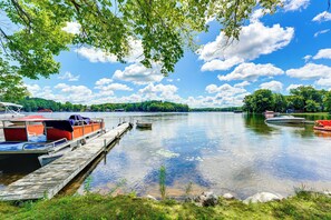 A calm lake with boats docked on a wooden pier, surrounded by lush greenery and a clear blue sky. - Waterfront Escape on Bass Lake: Paddle, Fish, Swim (Irons)