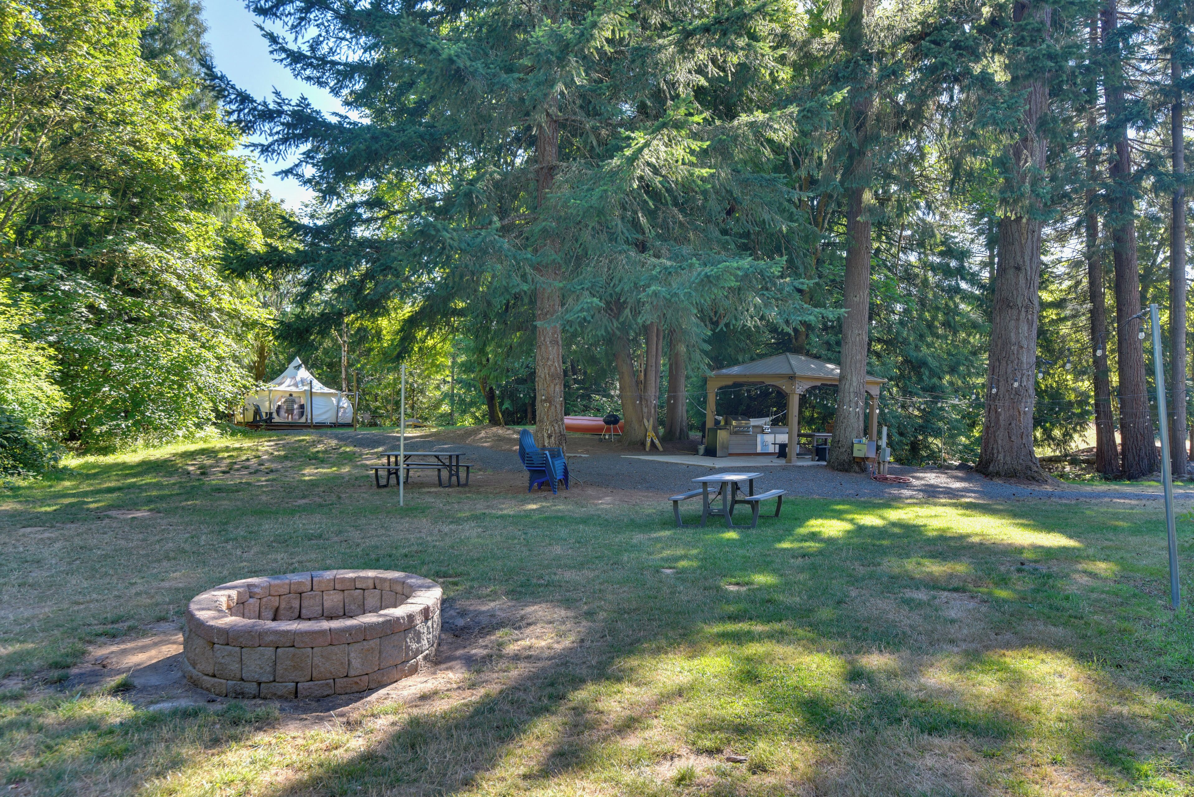 A campsite with picnic tables, a fire pit, a covered grill area, and a tent.