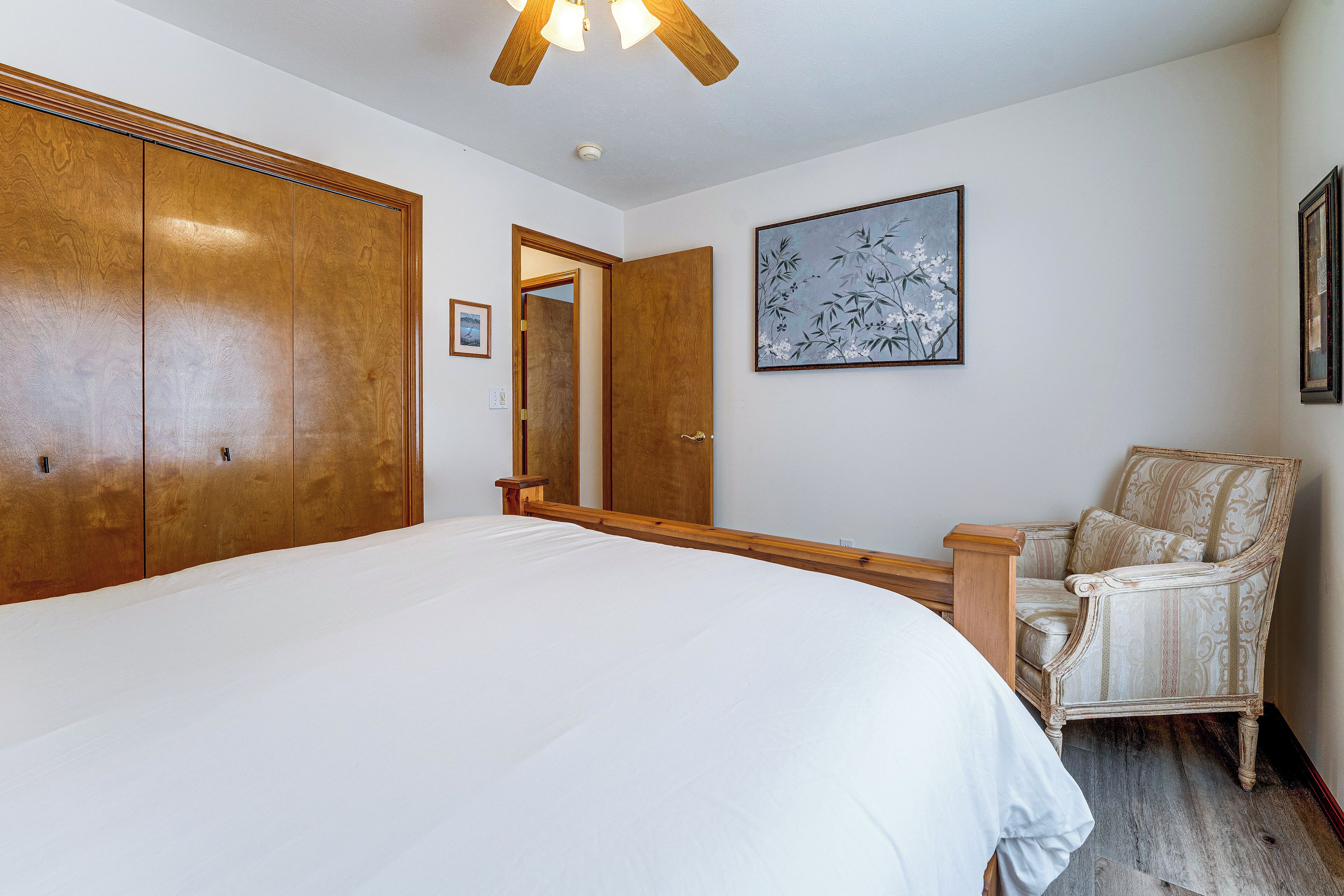 A bedroom with a large bed, wooden wardrobe, a chair, and a painting on the wall.