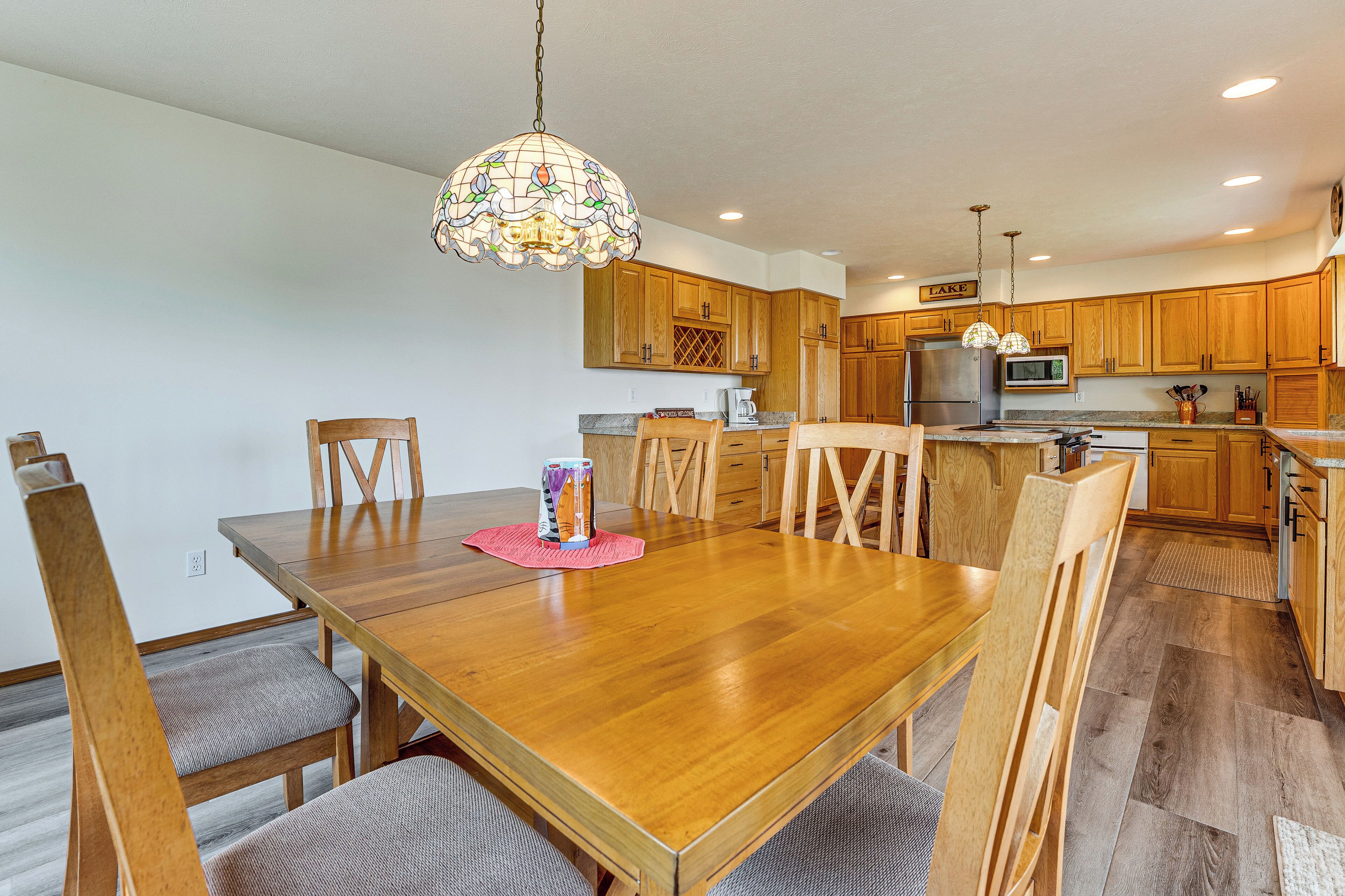 A dining area with a wooden table and chairs, a kitchen with wooden cabinets, and a hanging light fixture.