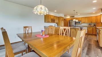 A dining area with a wooden table and chairs, a kitchen with wooden cabinets, and a hanging light fixture.