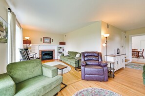A living room with a fireplace, green sofas, a leather armchair, and a dining area with a table and chairs. - Farmhouse W/creek & Fireplace Near Gettysburg! (Biglerville)