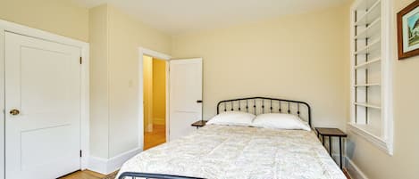 A bedroom with a bed, a nightstand, a door, and a window with blinds.