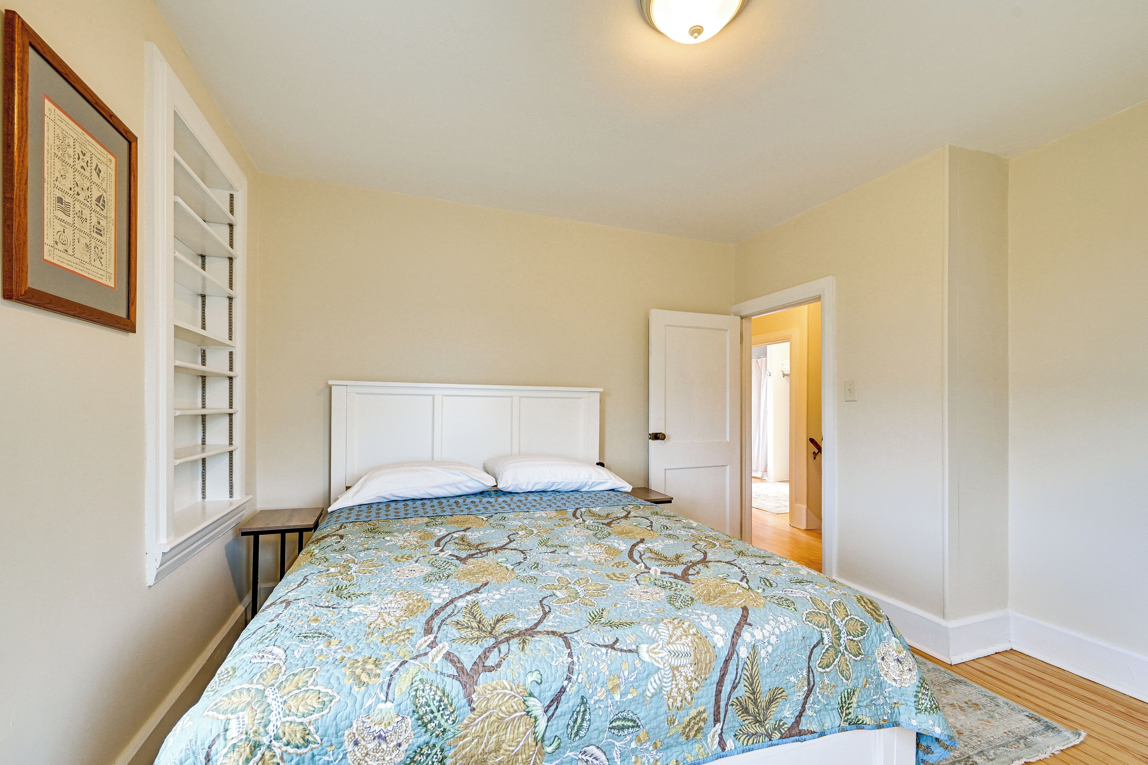 A bedroom with a bed, a nightstand, a door, and a wall-mounted shelf.