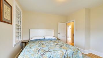 A bedroom with a bed, a nightstand, a door, and a wall-mounted shelf.