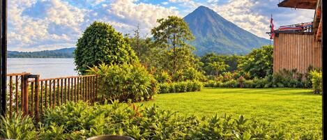 A view from a balcony with a mountain in the background, a wooden fence, and a grassy lawn.
