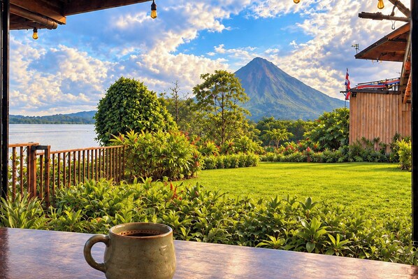 A view from a balcony with a mountain in the background, a wooden fence, and a grassy lawn.