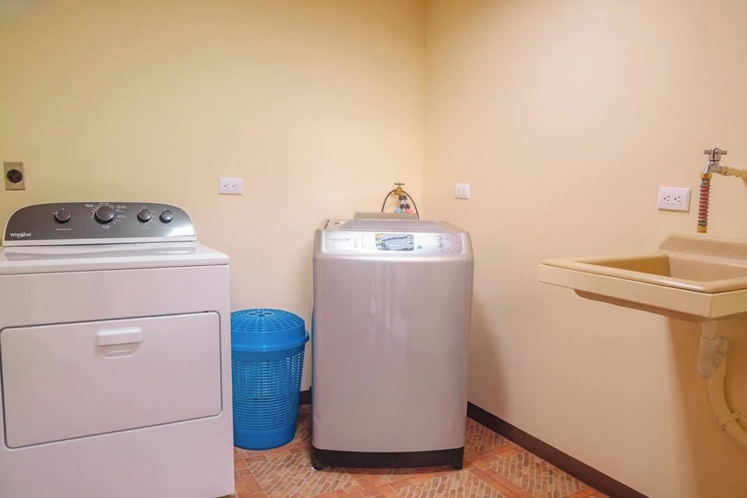A laundry room with a washing machine, a dryer, a blue laundry basket, and a sink.