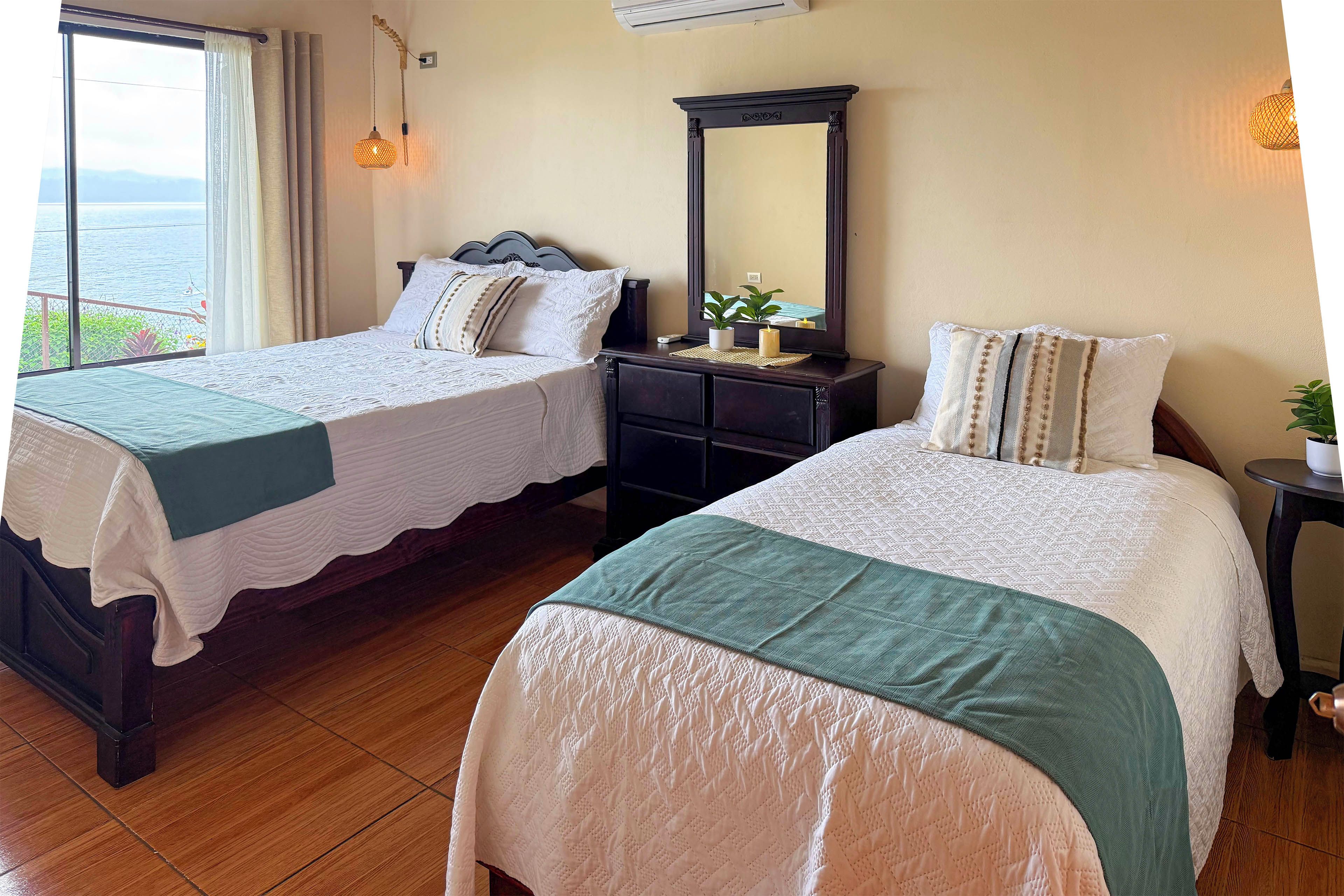 Une chambre d’hôtel avec deux lits, une commode, un miroir et une vue sur la mer.
