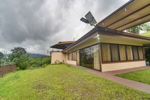 A modern house with a large glass window, a solar panel, and a grassy yard.