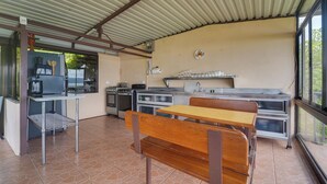 A covered outdoor kitchen area with a dining table and benches, a refrigerator, a stove, and a sink. - Home w/ Surrounding Lake Arenal & Volcano Views! (Peñas Blancas)
