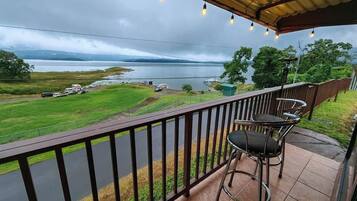 A balcony with a view of a lake, a chair, and a table.