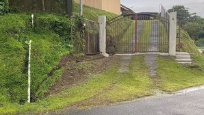 A gated entrance with a metal gate, a grassy area, and a paved path leading to a building. - Home w/ Surrounding Lake Arenal & Volcano Views! (Peñas Blancas)