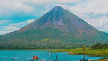 A mountain with a lake in the foreground, boats, and parked cars.