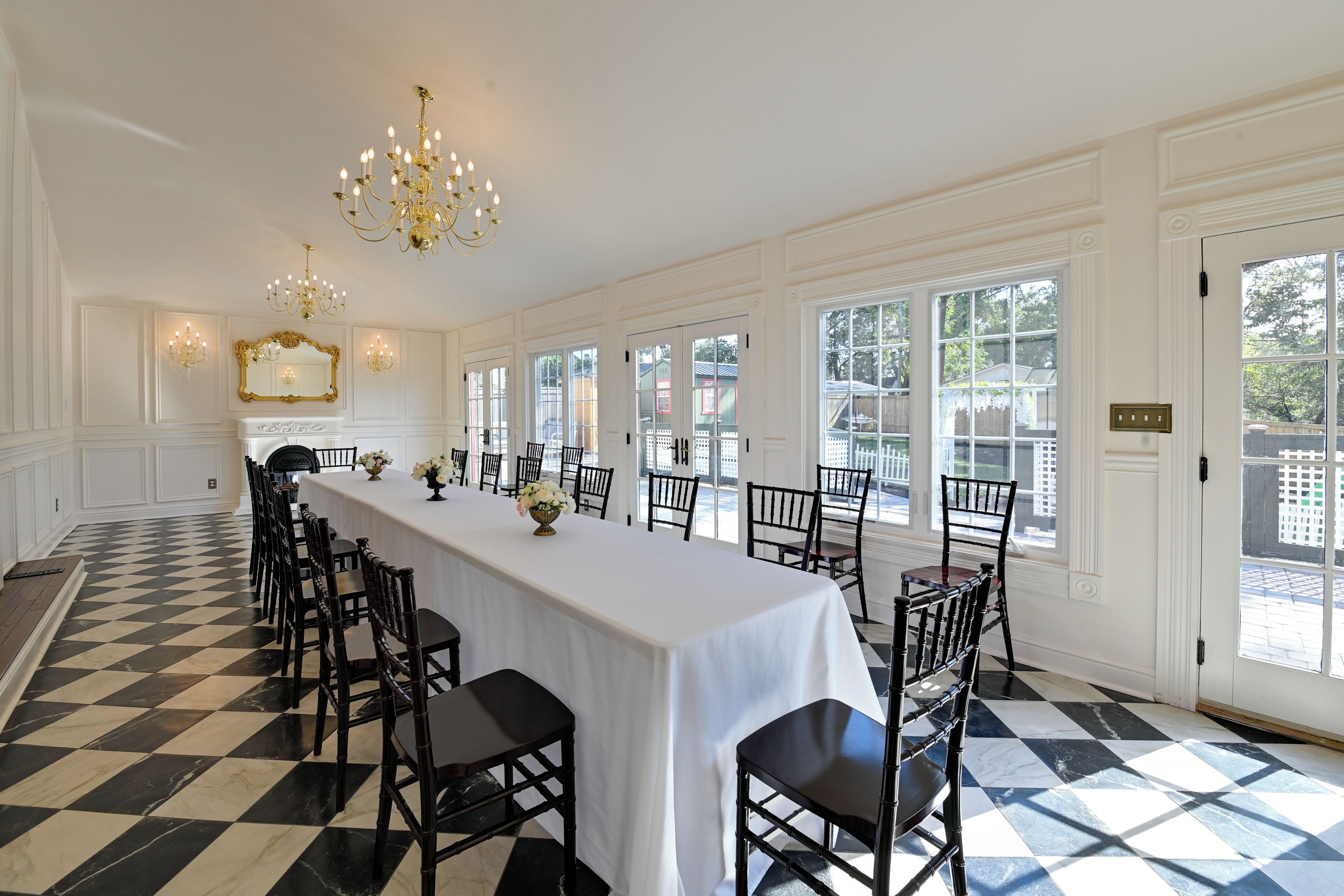 A long dining table with chairs, chandeliers, and a view of the outside.