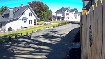 A residential street with houses, a white car parked on the side, and a wooden fence.