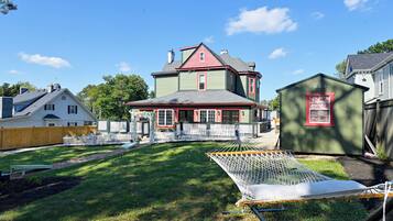 A large house with a red roof and green siding, surrounded by a white picket fence and a hammock.