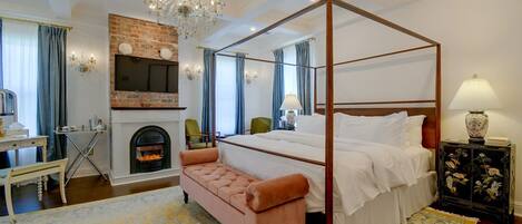 A four-poster bed with a fireplace, a bench, and a television in a hotel room.
