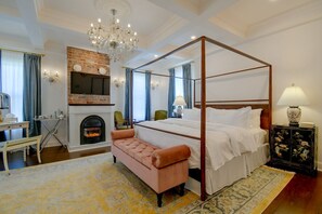 A four-poster bed with a fireplace, a bench, and a television in a hotel room.