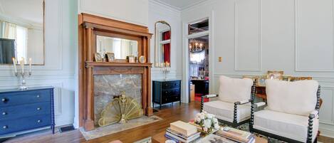 A well-appointed living room with a fireplace, a blue dresser, and two white armchairs.