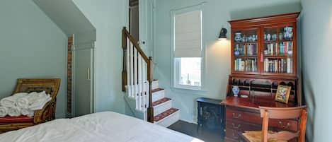 Un dormitorio con una cama, una silla de madera, una estantería, una chimenea y una escalera.