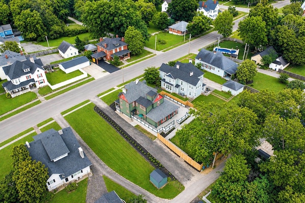 An aerial view of a residential area with multiple houses, a central road, and green lawns.