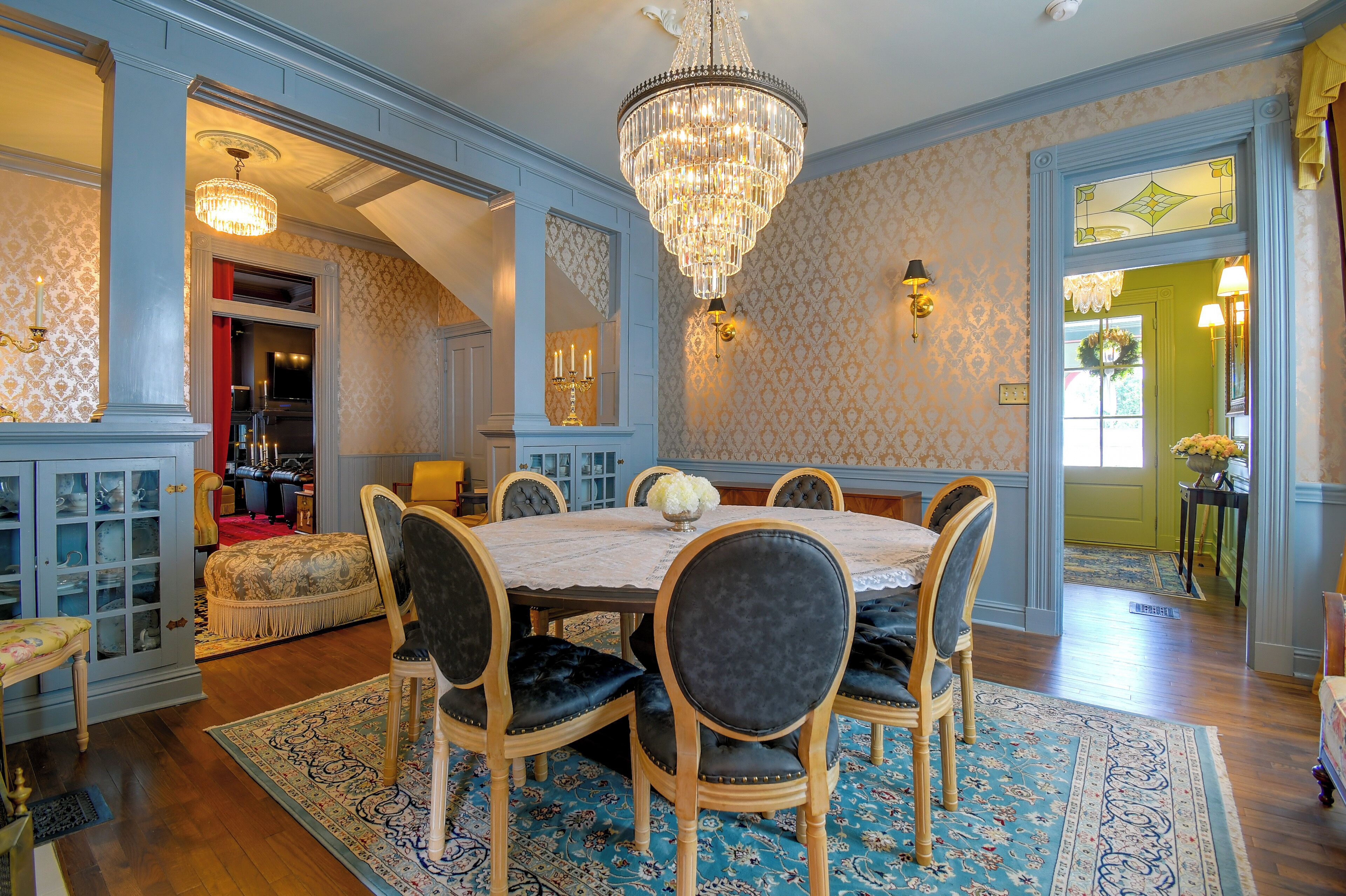 A dining room with a chandelier, patterned wallpaper, and a blue and gold color scheme.