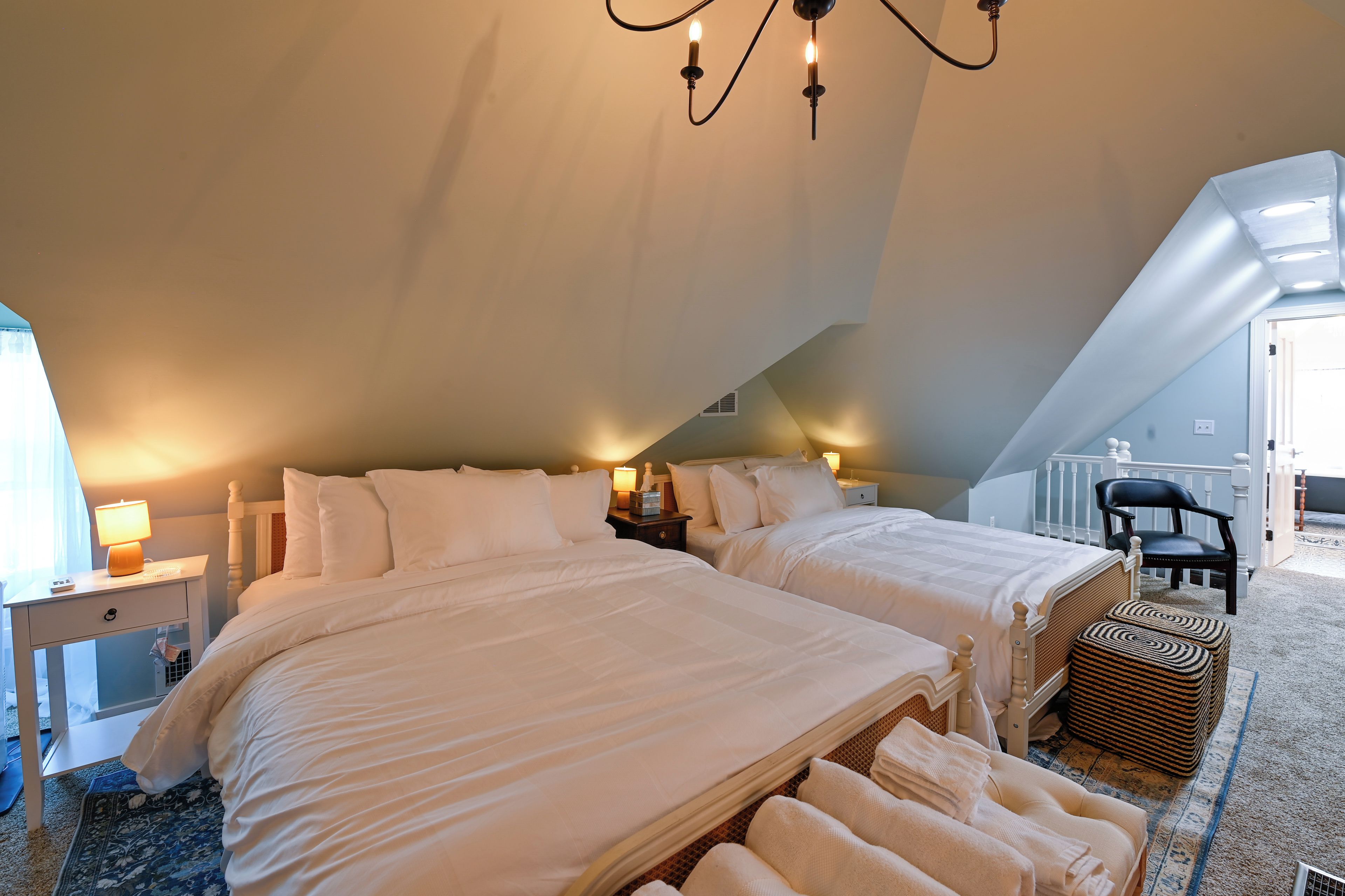 A bedroom with two beds, a chandelier, a chair, and a small table with a lamp.