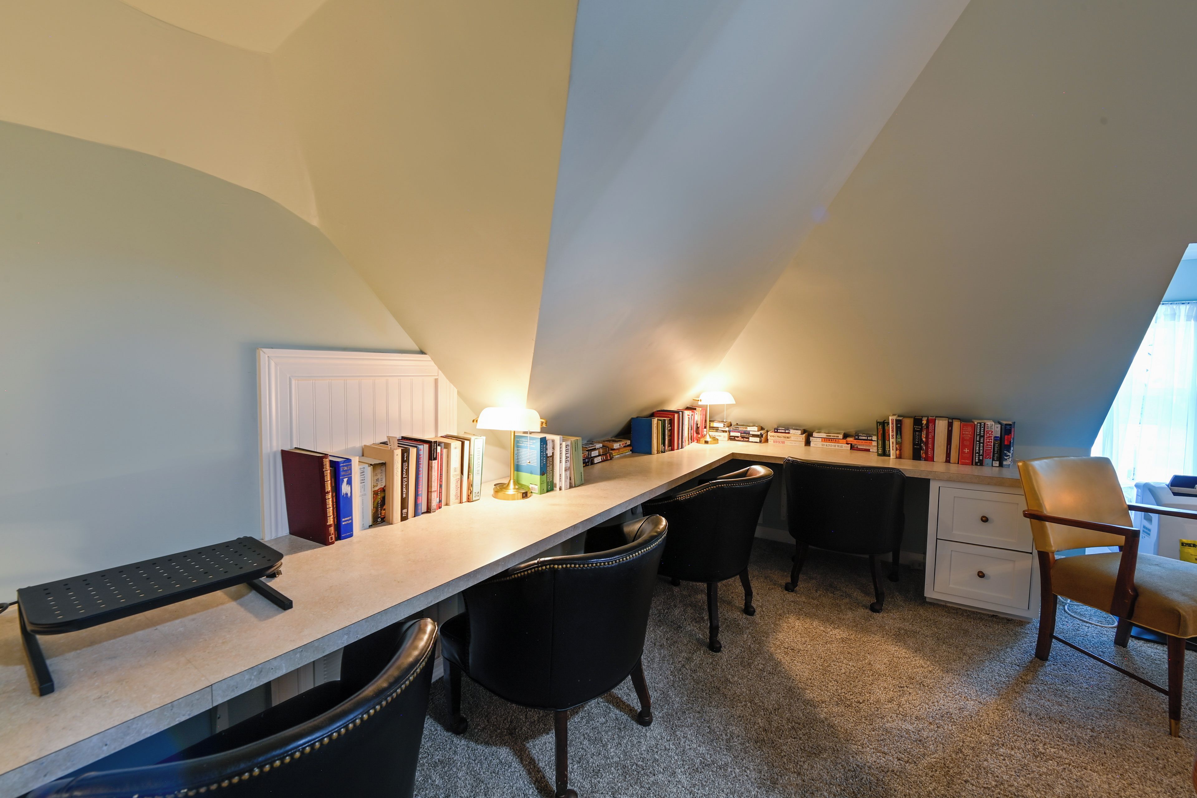 A study room with a desk, chairs, books, and a lamp.