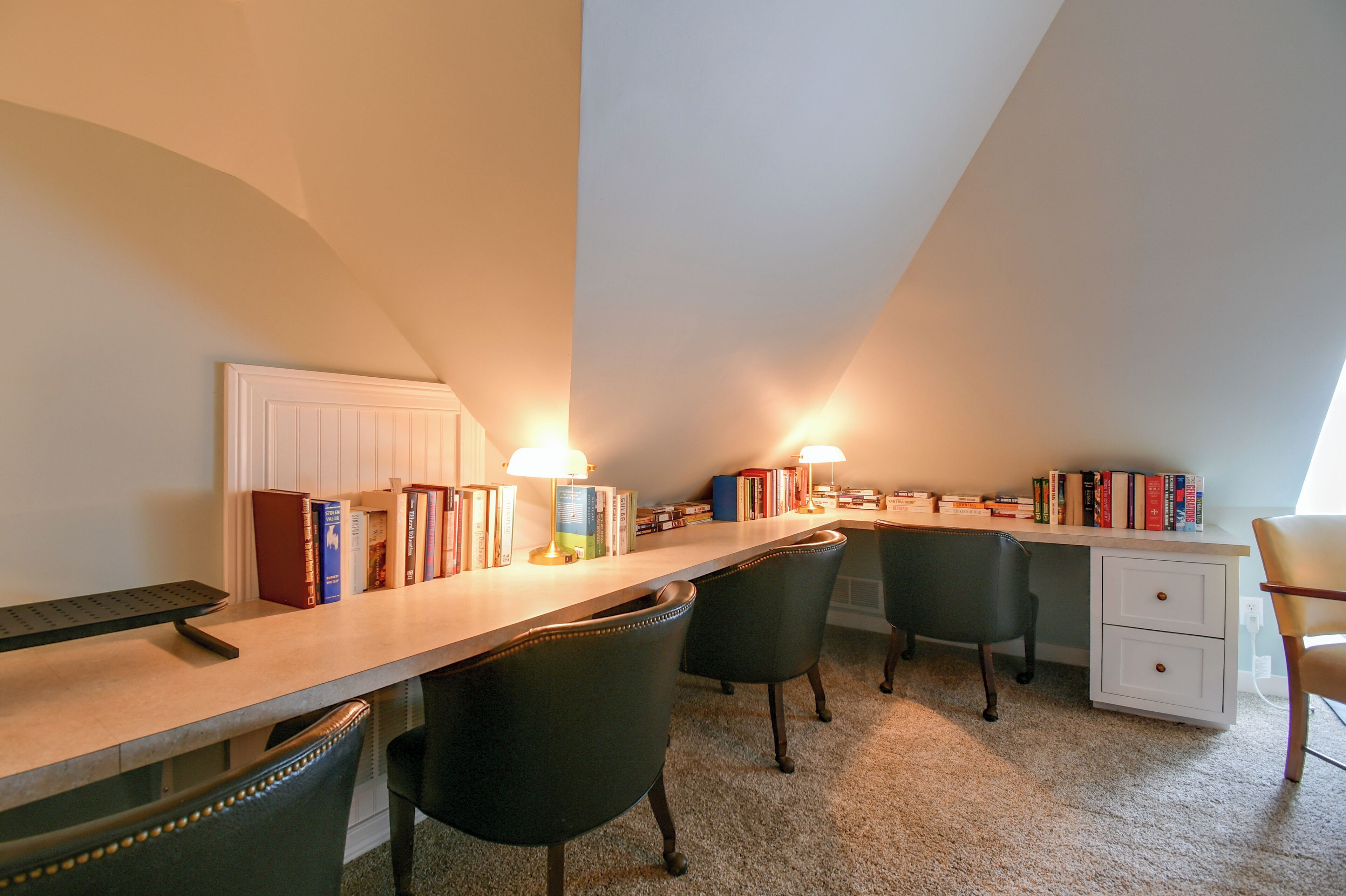 A study room with a desk, chairs, books, and two lamps.