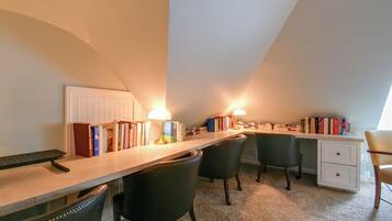 A study room with a desk, chairs, books, and two lamps.