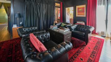 A dark-themed living room with a black leather sofa, a coffee table, and a red rug.