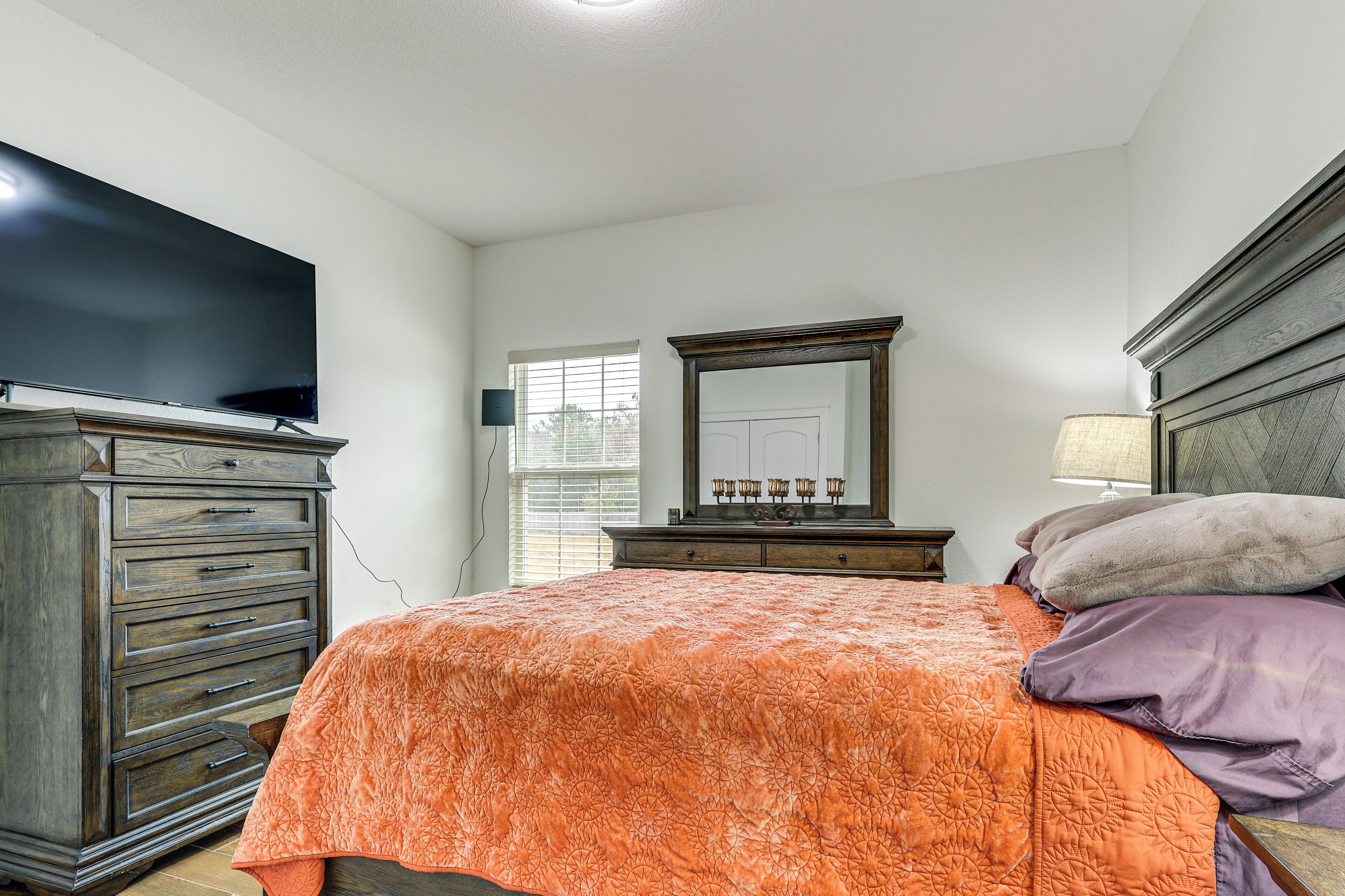 A bedroom with a bed, dresser, TV, and a window with blinds.