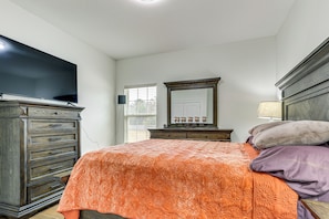 A bedroom with a bed, dresser, TV, and a window with blinds.